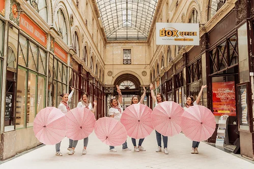 clip vidéo evjf à bordeaux avec groupe de femmes posant avec des parapluies roses dans une galerie couverte