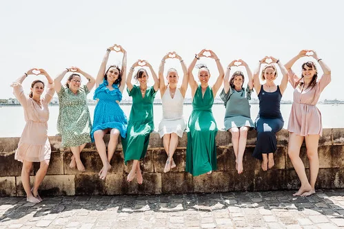 groupe de femmes assises sur un muret en robes colorées formant des coeurs avec leurs mains lors dun clip video evjf a la rochelle