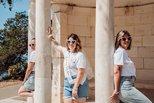 trois femmes en tshirts blancs et shorts posent avec des lunettes coeur autour dun pavillon en pierre 