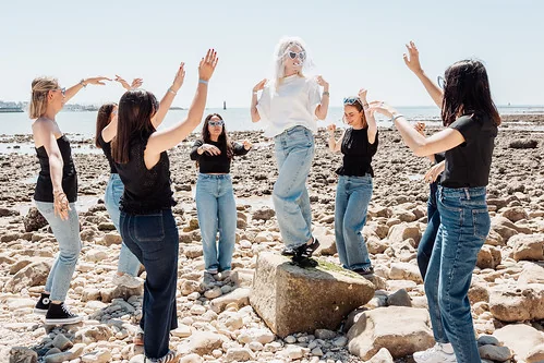 femme en tshirt blanc et voile debout sur un rocher entouree de ses amies en noir lors dun clip video evjf a la rochelle
