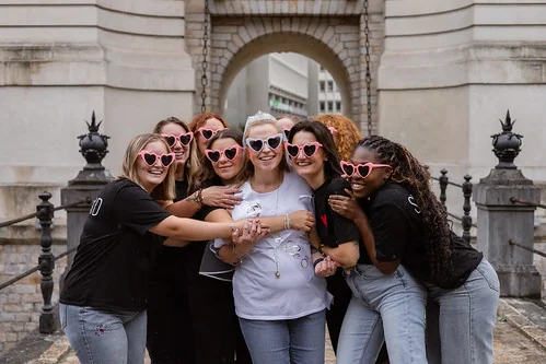 future mariee entouree de ses amies en lunettes roses coeur posant ensemble pendant un clip video evjf lille