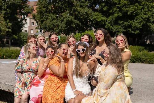 future mariee en robe blanche et ses amies en robes colorees posant avec des lunettes roses 