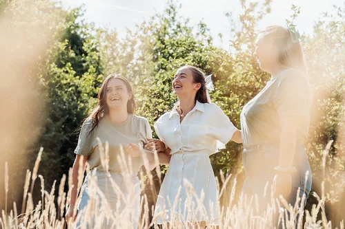 trois femmes riant ensemble dans un champ ensoleille pendant un clip video evjf a tours en pleine nature