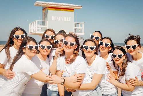 groupe de femmes en t shirt blanc et lunettes coeur posant ensemble sur la plage de deauville pour un evjf