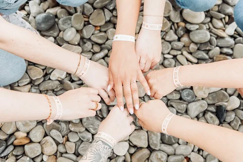 Mains de plusieurs amies portant des bracelets assortis posées ensemble sur des galets