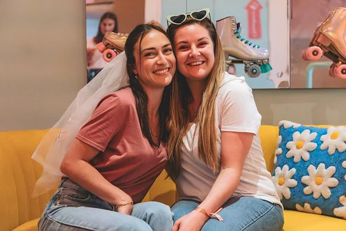  Deux amies souriantes assises sur un canapé, dont la future mariée avec un voile