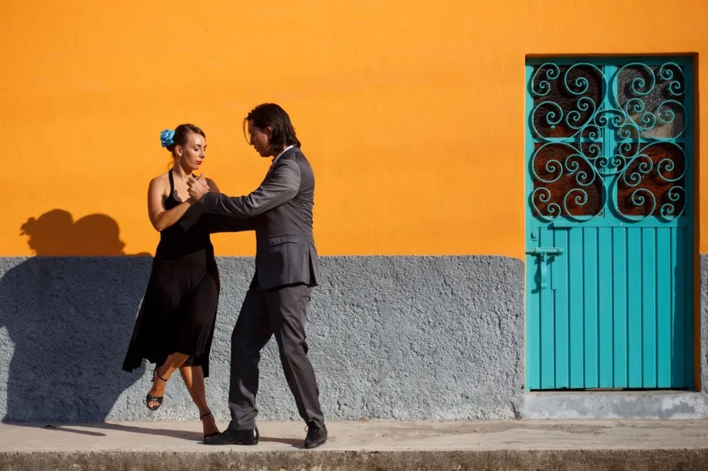 Couple dansant une danse latine dans une rue colorée avec un mur orange et une porte turquoise