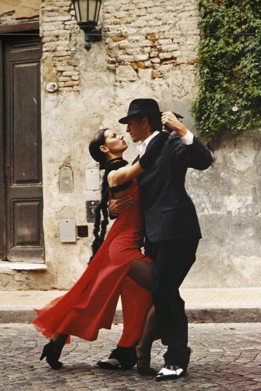 Couple exécutant une figure de tango en extérieur, la danseuse en robe rouge élégante