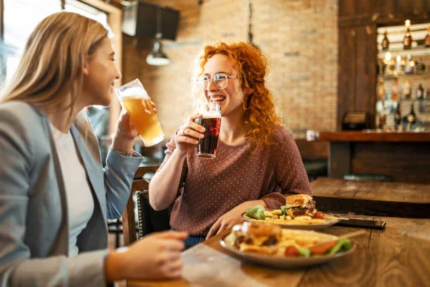Dégustation bières artisanales EVJF à Strasbourg, deux amies souriantes trinquent avec des pintes dans un bar convivial
