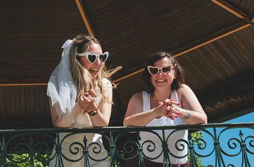future mariée et son amie portent des lunettes en forme de cœur et sourient lors d’un evjf à tours sous un kiosque ensoleillé