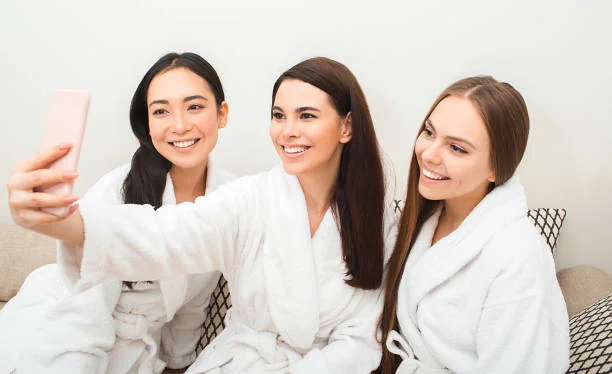 Trois femmes en peignoir blanc prenant un selfie souriant lors d’un evjf détente entre amies