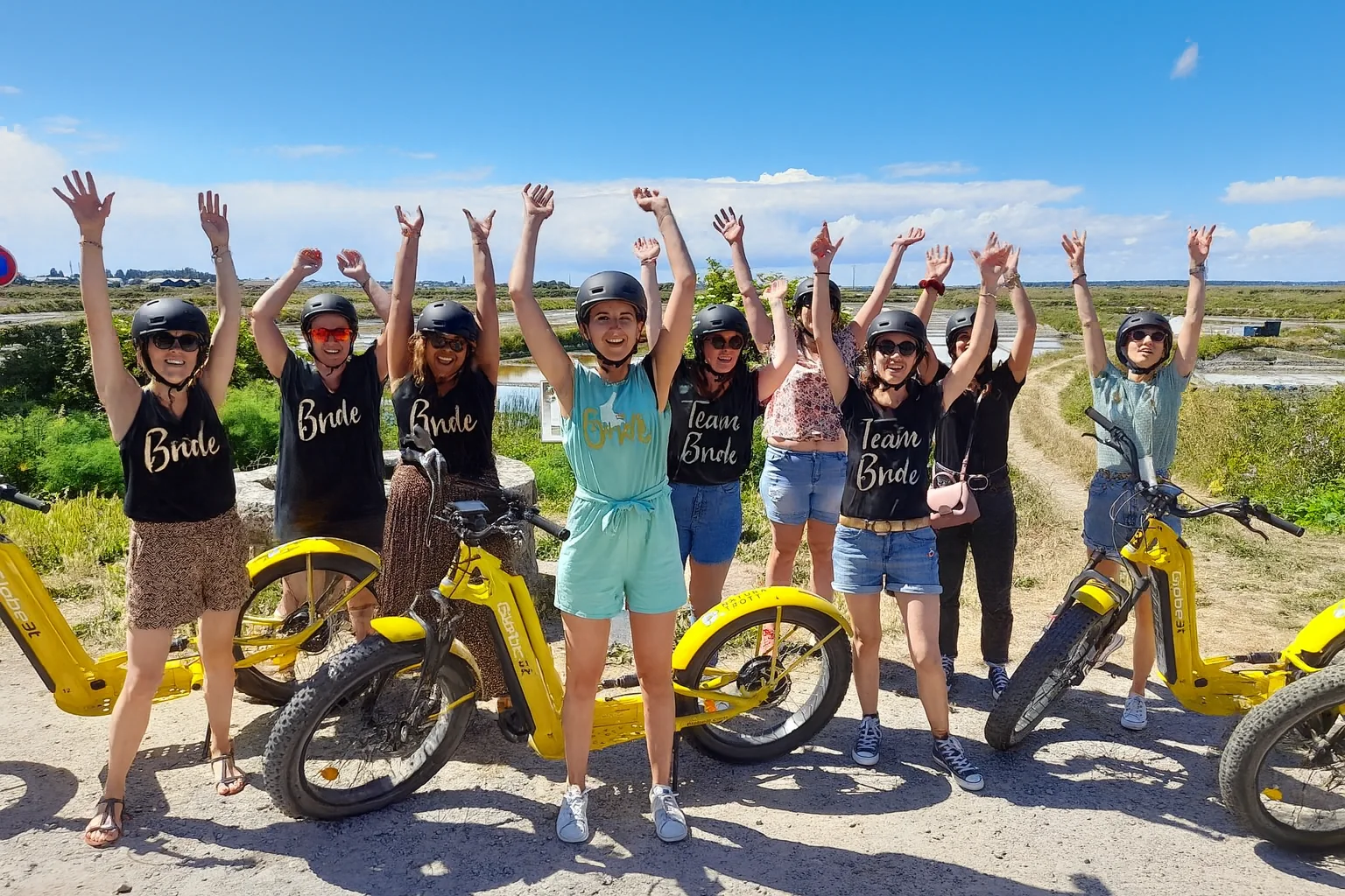 Groupe de jeunes femmes celebrant un EVJF avec des trottinettes electriques jaunes pres des marais salants.