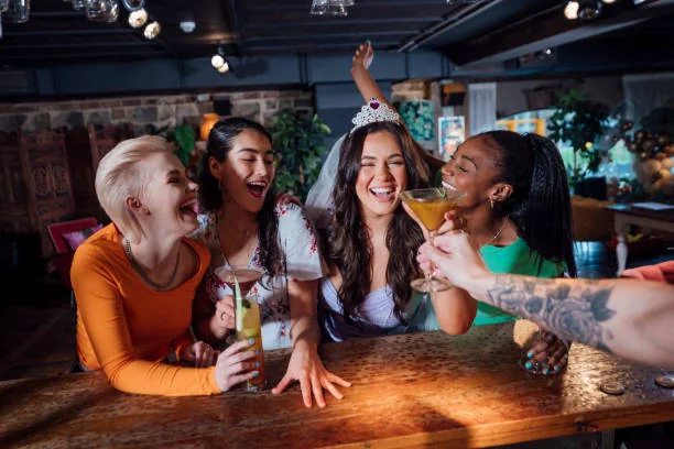 Groupe de femmes riant autour d’un bar et partageant des cocktails avec la future mariée
