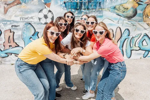 groupe de femmes souriantes en lunettes coeur pose devant un mur graffite 