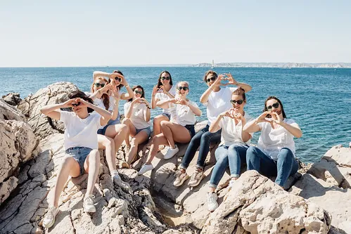 groupe de femmes assises sur des rochers faisant des coeurs avec les mains en bord de mer 
