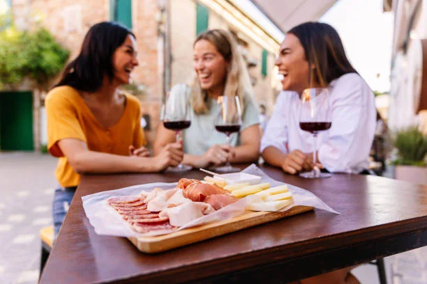 trois femmes rient autour d un verre de vin et d une planche de charcuterie lors d un food tour pour un evjf a montpellier