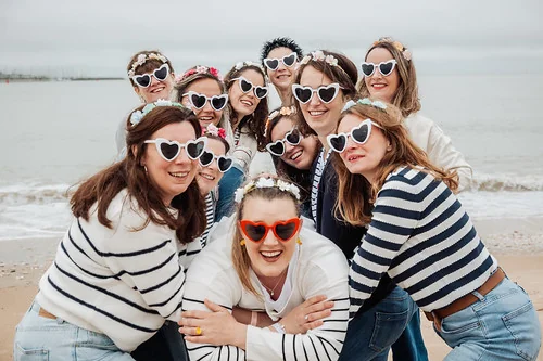 groupe de femmes en mariniere et lunettes coeur pose souriant sur la plage 