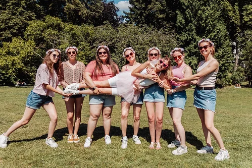 Amies portant la future mariée en robe blanche et lunettes roses lors d’un koh lanta evjf à Rouen dans un parc