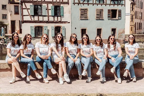 Groupe de femmes en t-shirt et jean posant ensemble à Strasbourg lors d un evjf, devant des maisons traditionnelles