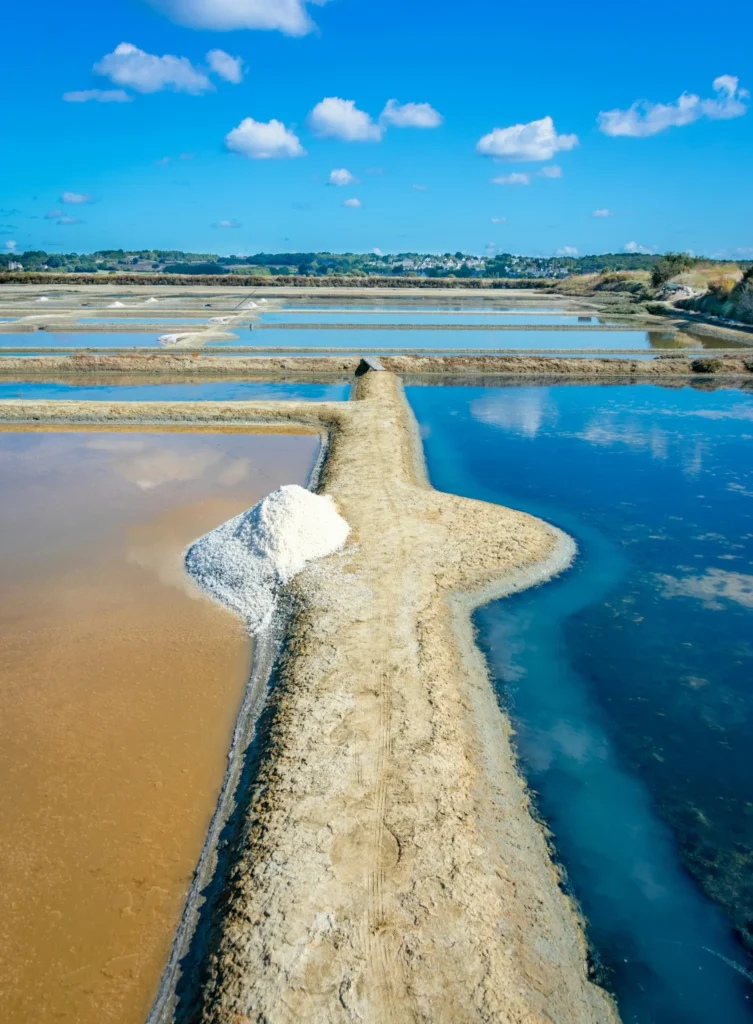 Vue panoramique des marais salants de Guerande avec tas de sel et bassins reflechissant le ciel bleu.