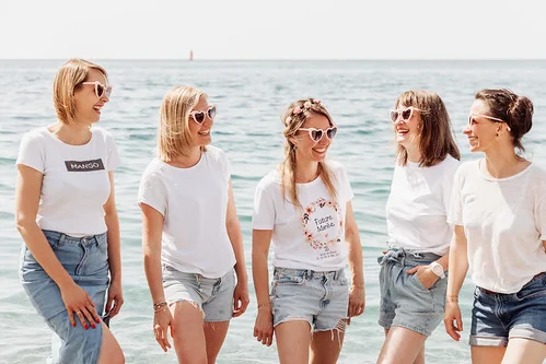 Pourquoi choisir un clip vidéo EVJF à Nice ? Six amies en short et t-shirt blanc rient ensemble en bord de mer
