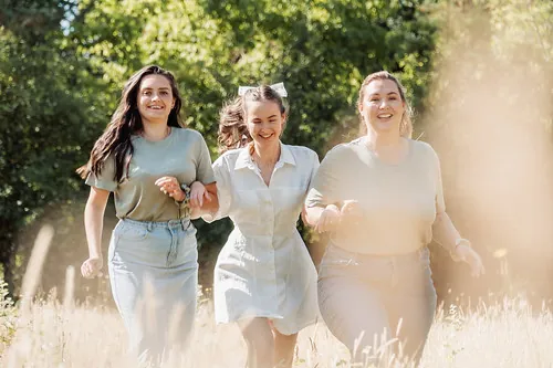 trois femmes souriantes courent main dans la main dans un champ ensoleillé à Tours, illustrant quand organiser un evjf à tours