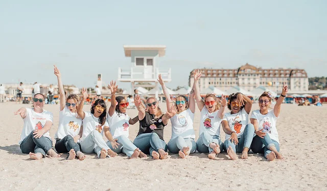 groupe de femmes en t shirt evjf assises sur la plage de deauville levant les bras pour reserver clip video evjf deauville