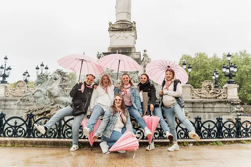 reservez shooting photo evjf à bordeaux : groupe de femmes avec parapluies roses posant devant la fontaine des girondins
