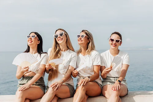 Comment se déroule une séance photo à Nice ? Quatre amies en t-shirt blanc et lunettes cœur posent souriantes en bord de mer