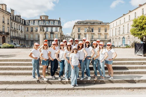 shooting photo evjf à bordeaux activité tendance : grand groupe de femmes en tee-shirts blancs et casquettes rouges posant sur des marches