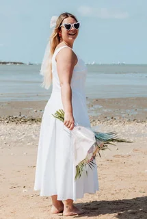 femme en robe blanche et lunettes coeur tenant un bouquet sourit sur la plage lors dun shooting photo evjf a la rochelle