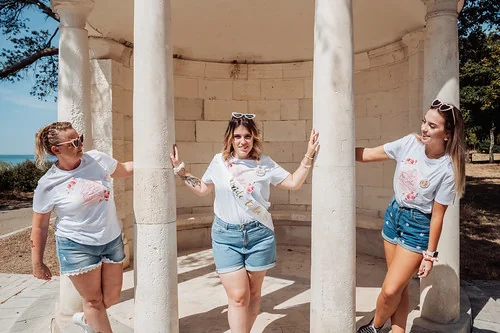 trois femmes en short et t shirts blancs posent sous un pavillon en pierre lors dun shooting photo evjf a la rochelle