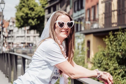 Future mariée souriante avec lunettes en cœur lors d’un shooting photo EVJF à Strasbourg, posant sur un pont pittoresque