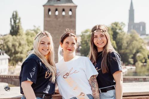 Trois amies souriantes lors d’un shooting photo EVJF à Strasbourg, posant sur un pont avec la cathédrale en arrière-plan
