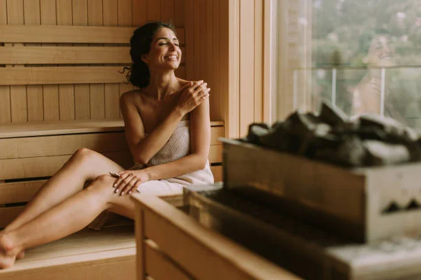 Femme souriante assise dans un sauna en bois, enveloppée d’une serviette, profitant d’un moment de bien-être lors d’un spa EVJF à Nantes.