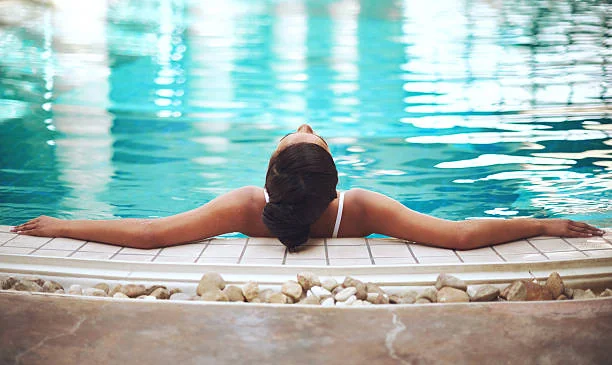 Femme en maillot se détend au bord d’une piscine intérieure, les bras étendus, lors d’un spa EVJF à Nantes.