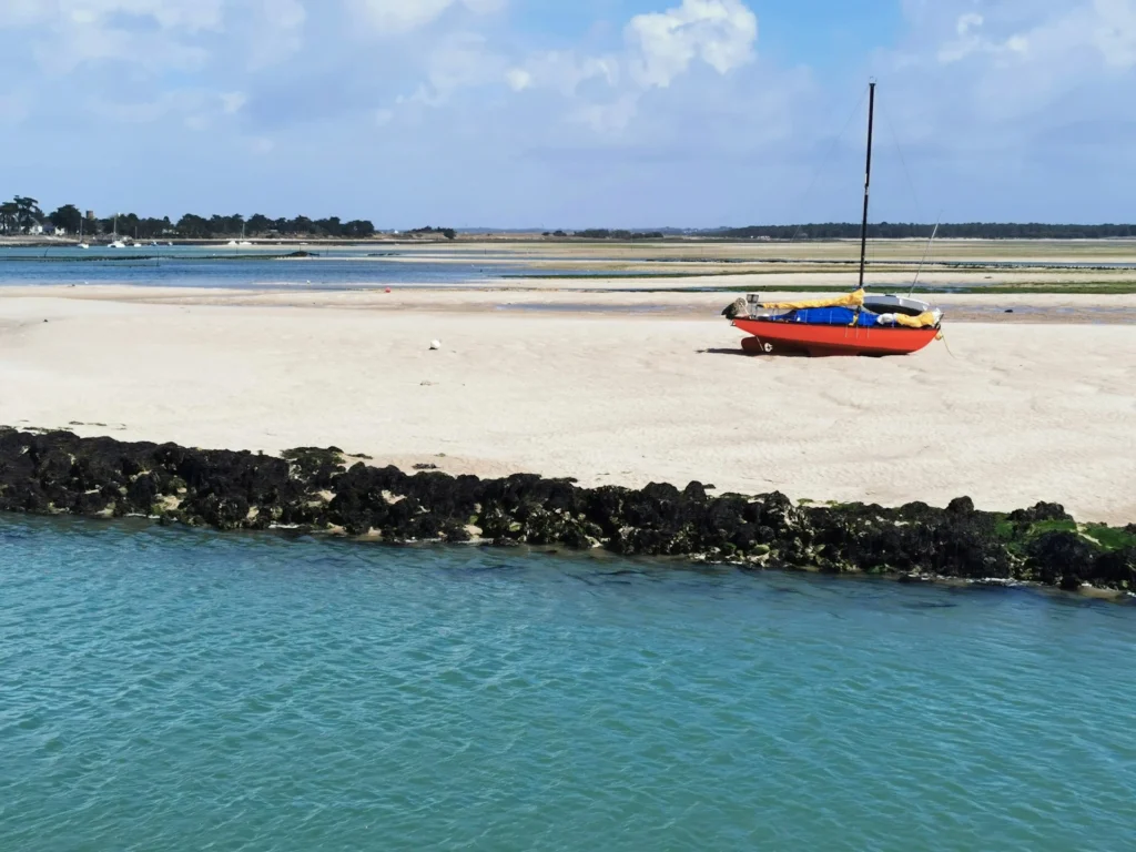 Petit voilier rouge échoué sur une plage de sable à marée basse dans la baie de La Baule.