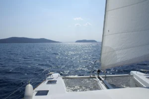 Vue avant d’un catamaran en navigation sur une mer calme et ensoleillée avec des îles au loin.