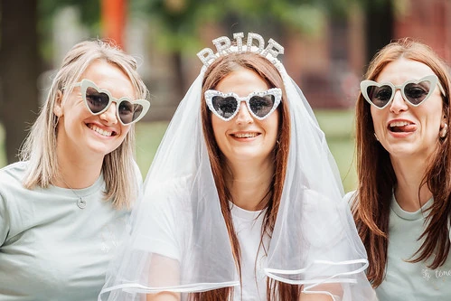 mariee avec voile et lunettes coeur entouree de ses amies souriantes illustrant 10 bonnes raisons pour faire un evjf a lille