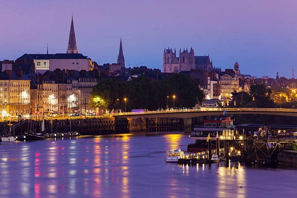 Vue nocturne du centre-ville de Nantes avec la cathédrale et les lumières se reflétant sur la Loire