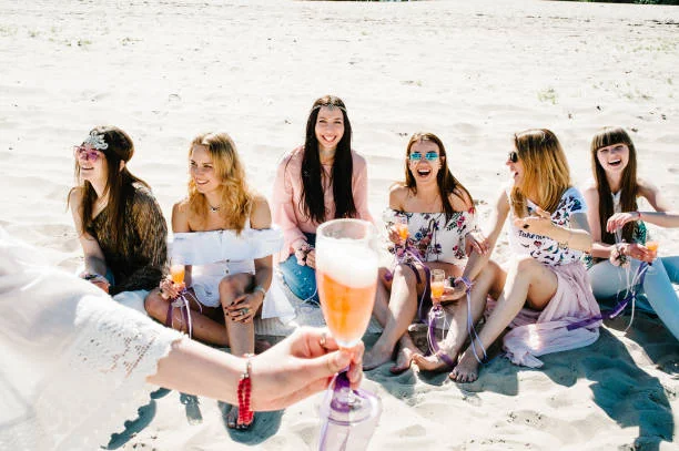 groupe de femmes assises sur la plage riant et tenant des verres pendant un evjf à montpellier