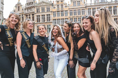 Team Bride souriante lors d un city game evjf a Bruxelles sur la Grand-Place, la mariee au centre en blanc