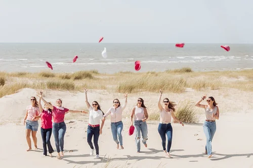 groupe de copines participant a un city game evjf le touquet en courant sur la plage et lançant des chapeaux en l air