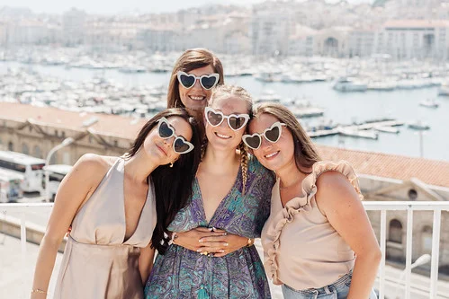 groupe de copines souriantes en lunettes coeur posant au vieux port pendant un city game evjf marseille