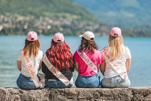 Quatre filles de dos avec des écharpes team bride assises face au lac lors d’un clip video evjf annecy