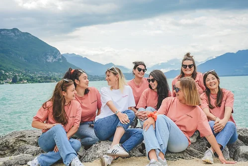 Groupe de filles assises sur les rochers au bord du lac, souriantes lors d’un clip video evjf annecy