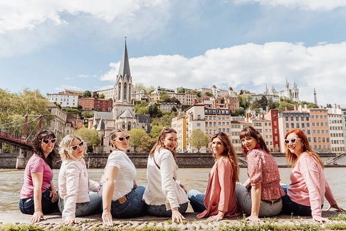 groupe de filles assises au bord de la saone posant pour clip video evjf lyon avec vue sur la ville