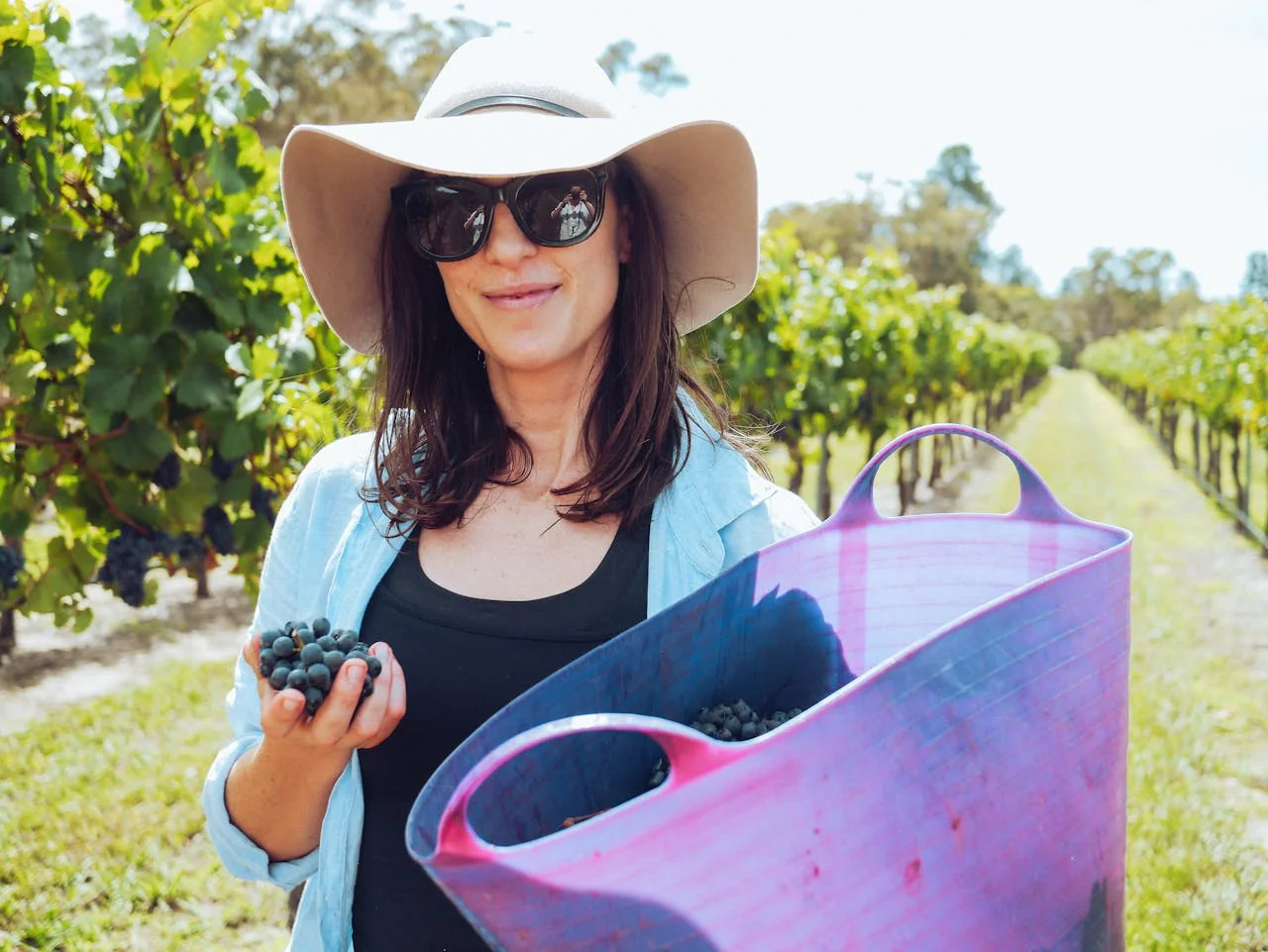Femme souriante tenant des grappes de raisin dans un vignoble lors d’un atelier vigneron à Paris