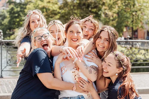 la future mariée entourée de ses amies qui rient et la serrent dans leurs bras