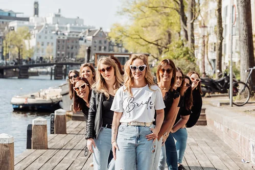 groupe de femmes souriantes en ligne pendant un jeu de piste evjf paranormal à amsterdam sur un quai au bord d’un canal
